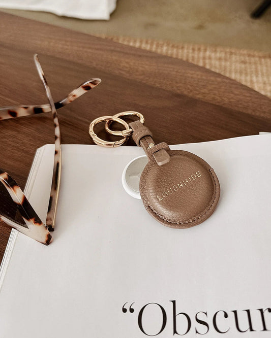 Brown leather keychain on a book with sunglasses and a woven mat in the background