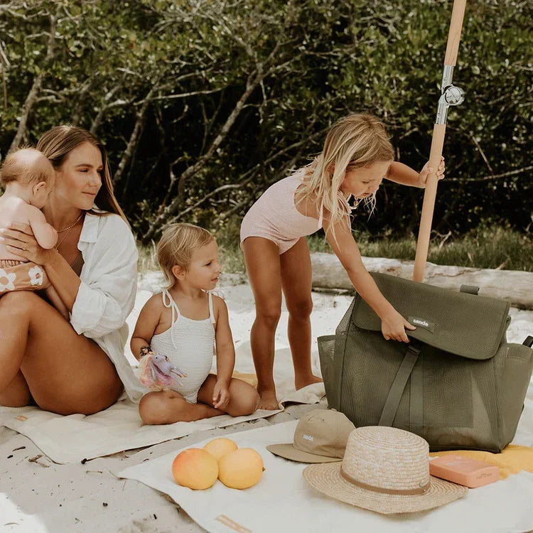 A family enjoying a beach picnic beside a green Sande Beach Hauler Backpack.
