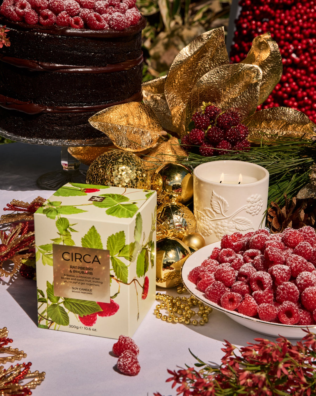 Raspberry & Rhubarb candle and botanical gift box styled with raspberry desserts and gold Christmas decorations.